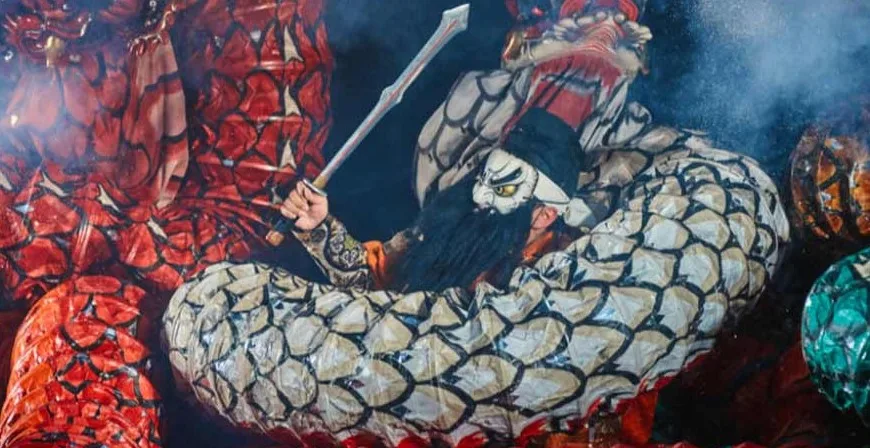 kagura dance with a Japanese dragon and a man wearing a white mask and beard. He raises a sword in his hand.